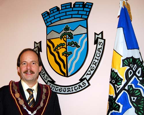 Town of Halton Hills Mayor Rick Bonnette beside the crest and flag of the Town